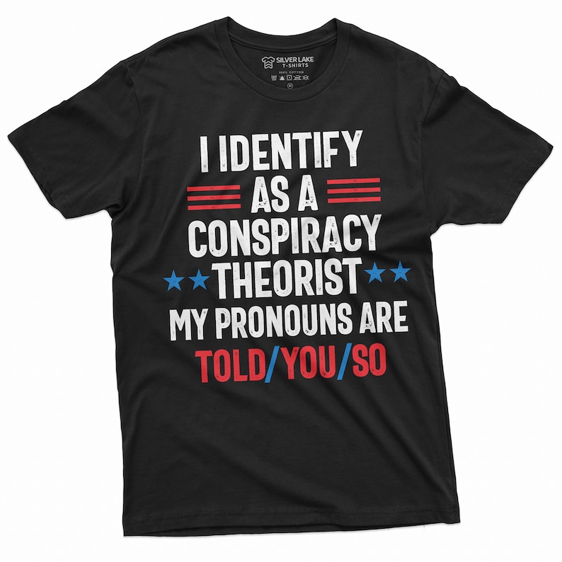 May include: Black t-shirt with a white graphic that says "I identify as a conspiracy theorist. My pronouns are told/you/so". The graphic also includes three red stripes, two blue stars, and the text is in a distressed font.