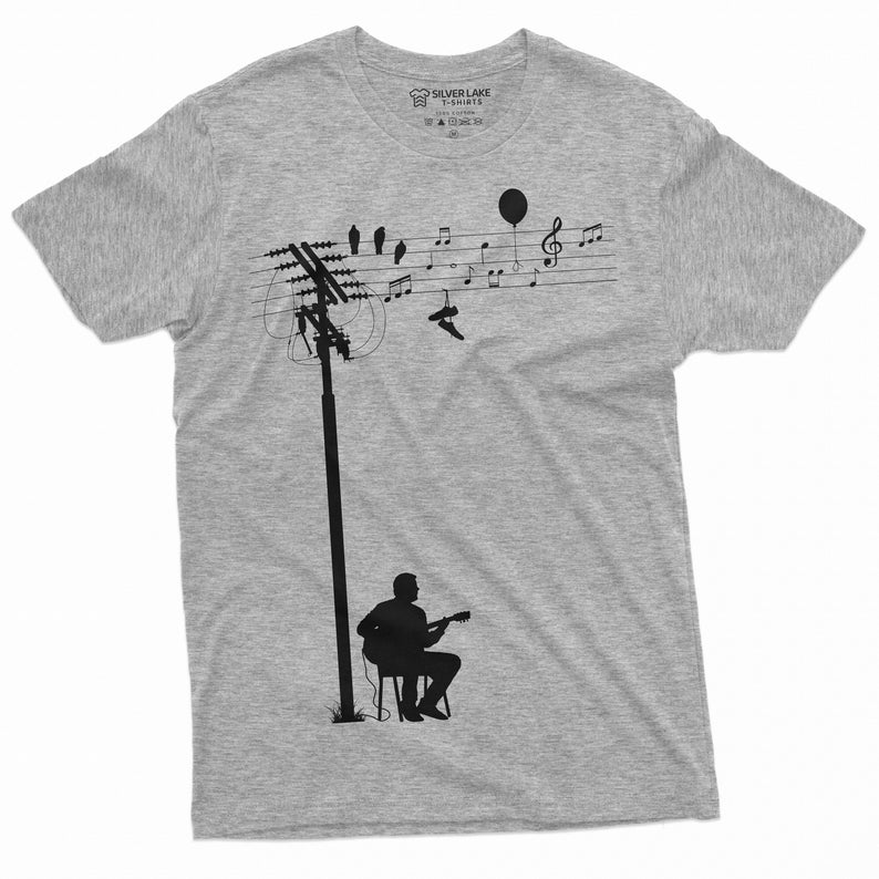 K&ouml;nnte beinhalten: Ein graues T-Shirt mit einer schwarzen Silhouette einer Person, die Gitarre spielt unter einer Stromleitung mit V&ouml;geln und Noten. Das Etikett lautet "Silver Lake T-Shirts".