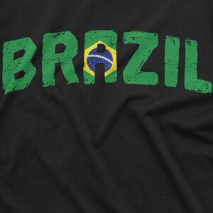 Puede incluir: Camiseta negra con un gr&aacute;fico desgastado verde y amarillo de la palabra "BRAZIL" con la bandera brasile&ntilde;a en el medio.