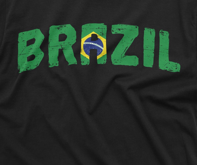 Puede incluir: Camiseta negra con un gr&aacute;fico desgastado verde y amarillo de la palabra "BRAZIL" con la bandera brasile&ntilde;a en el medio.