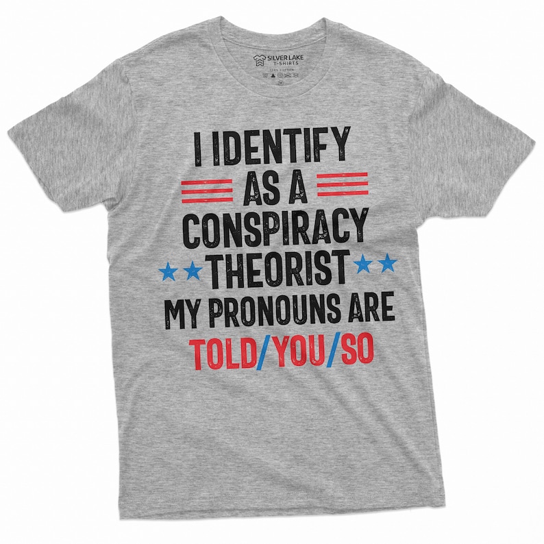 May include: Gray t-shirt with the text "I identify as a conspiracy theorist. My pronouns are told/you/so" in black with red and blue accents.