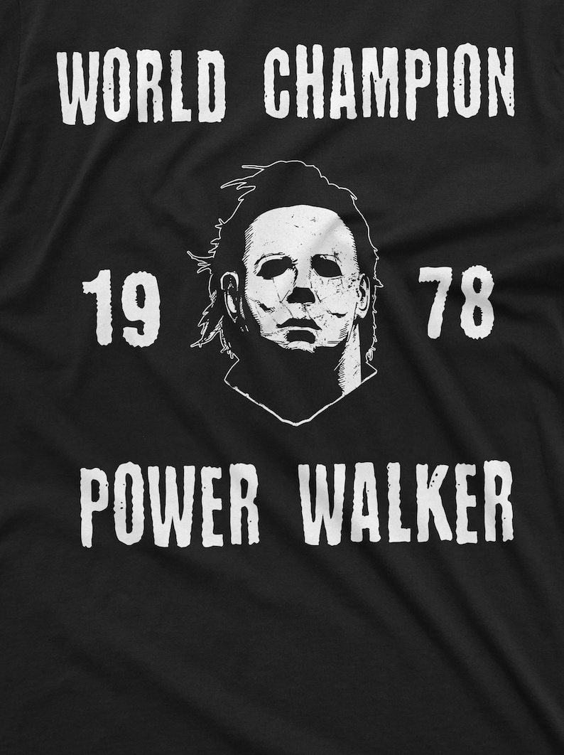 May include: Black and white graphic t-shirt featuring a white image of a masked figure and the text "WORLD CHAMPION 19 78 POWER WALKER".