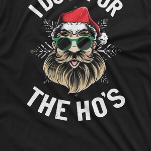 May include: A black t-shirt with a white graphic of Santa Claus wearing sunglasses and a beard. The text "I do it for the ho's" is printed in white below the graphic.