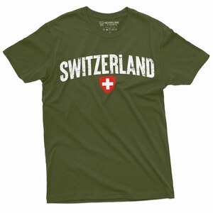 May include: A green t-shirt with the word "SWITZERLAND" printed in white with a distressed look. The Swiss flag is printed in red and white below the word.