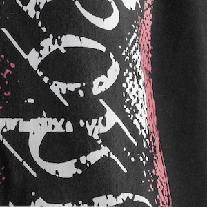 May include: Black t-shirt with a white and pink graphic print. The print features a stylized design with a distressed look.