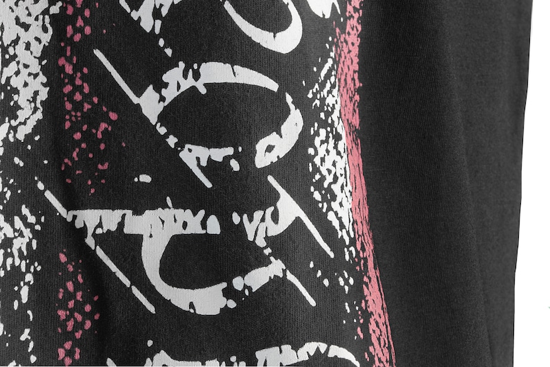 May include: Black t-shirt with a white and pink graphic print. The print features a stylized design with a distressed look.