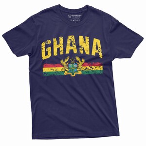 May include: A navy blue t-shirt with a distressed yellow graphic of the word "GHANA" and the Ghanaian flag with its coat of arms.