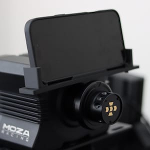 Può includere: Base del volante del simulatore di corse nera con un supporto per telefono. La base del volante ha la scritta "MOZA RACING". Il volante ha un design nero e oro.