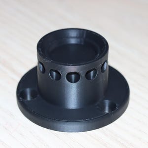 以下が含まれることがあります： 黒いプラスチック製の円筒形の物体で、円形のベースと上部の開口部があります。円筒には、周囲に等間隔に配置されたいくつかの穴があります。物体は明るい色の木製の表面に置かれています。