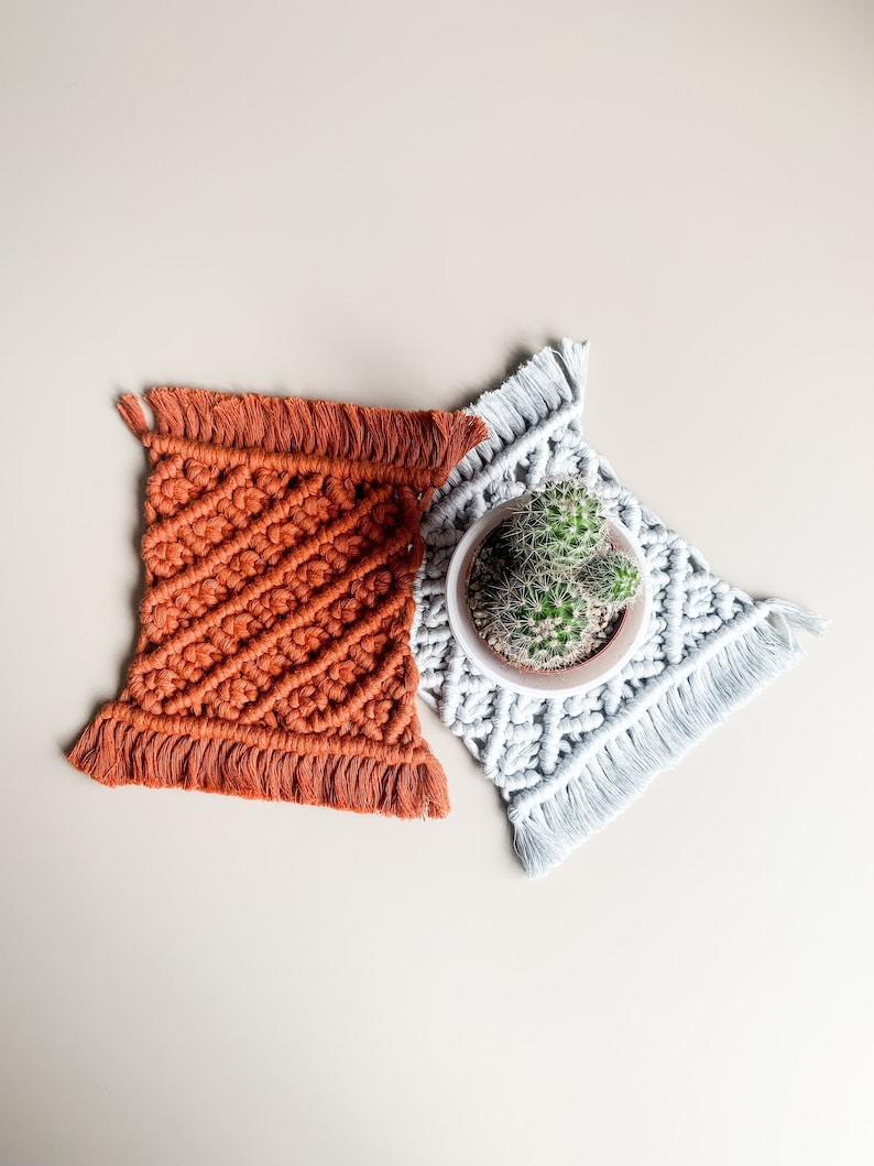 Peut inclure: Deux sous-verres en macram&eacute; faits &agrave; la main, l'un en orange et l'autre en blanc, avec un petit cactus en pot au centre.