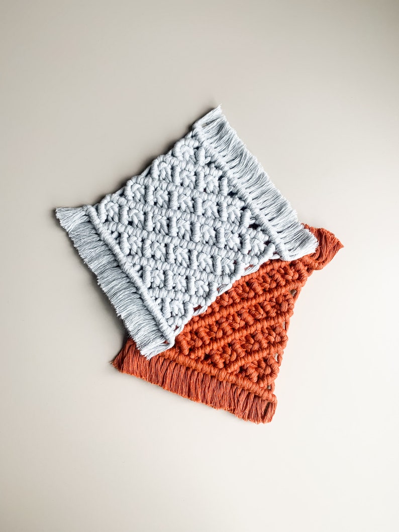 Peut inclure: Deux dessous-de-verre en macram&eacute; faits &agrave; la main, l'un de couleur gris clair et l'autre de couleur orange br&ucirc;l&eacute;. Les deux dessous-de-verre ont une bordure en franges.