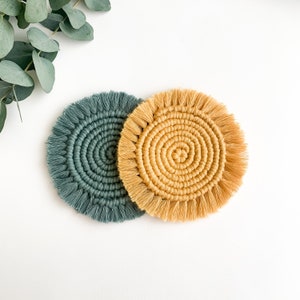 May include: Two round crocheted coasters, one in a deep green color and the other in a light yellow color. Both coasters have a fringe around the edge.