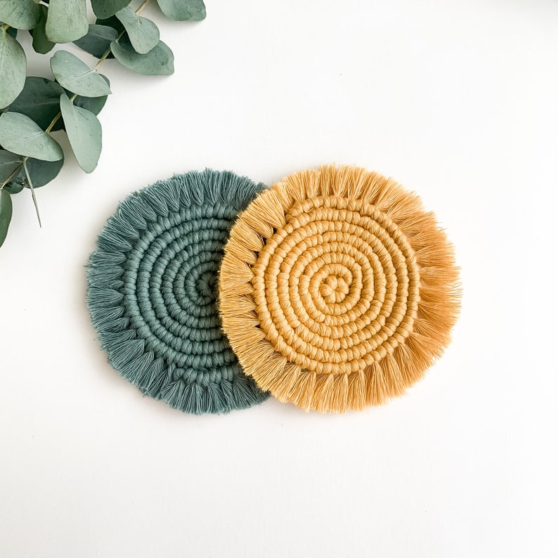 May include: Two round crocheted coasters, one in a deep green color and the other in a light yellow color. Both coasters have a fringe around the edge.