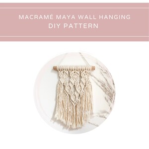 May include: A white macrame wall hanging with a wooden dowel at the top. The hanging features a repeating diamond pattern.
