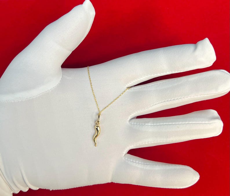 May include: A gold necklace with a small, detailed, gold horn pendant. The necklace is on a white surface.