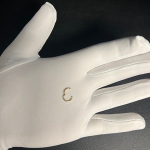May include: A small gold hoop earring, shown on a white gloved hand.