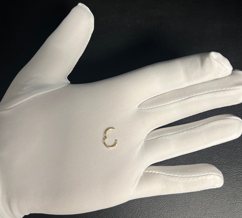 May include: A small gold hoop earring, shown on a white gloved hand.