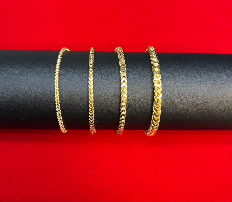 May include: Four gold-colored chain bracelets with a textured, herringbone pattern.
