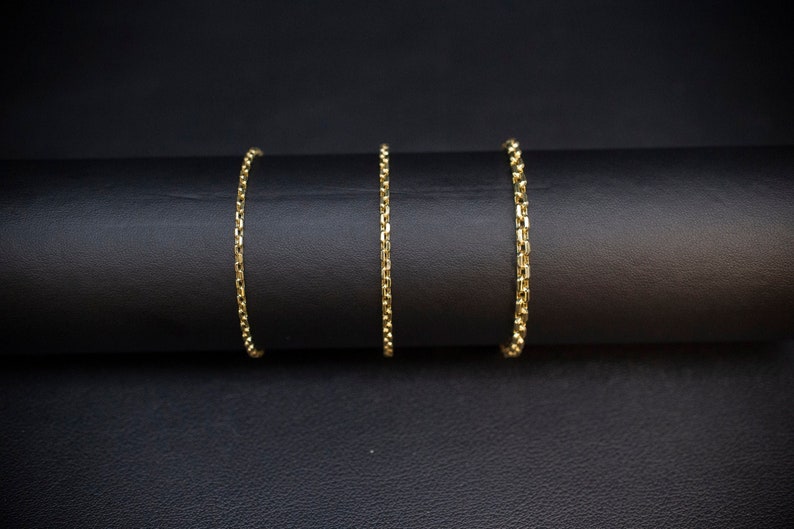 May include: Three gold chains of varying lengths on a black surface.