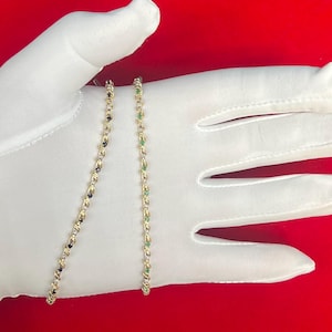 May include: Two gold chains with gemstones. One chain has green gemstones and the other has black gemstones.