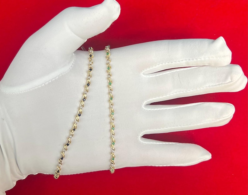 May include: Two gold chains with gemstones. One chain has green gemstones and the other has black gemstones.