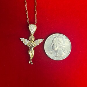 Puede incluir: Un collar de cadena de oro con un peque&ntilde;o colgante de &aacute;ngel detallado. El &aacute;ngel tiene las manos juntas en oraci&oacute;n y un halo de peque&ntilde;as piedras transparentes. El colgante es aproximadamente del tama&ntilde;o de una moneda de 25 c&eacute;ntimos de euro.