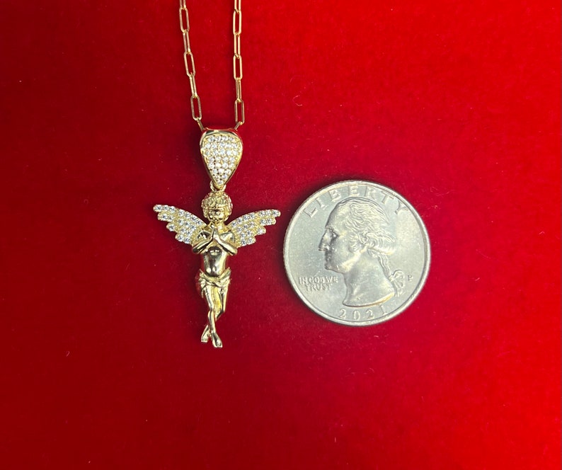 Puede incluir: Un collar de cadena de oro con un peque&ntilde;o colgante de &aacute;ngel detallado. El &aacute;ngel tiene las manos juntas en oraci&oacute;n y un halo de peque&ntilde;as piedras transparentes. El colgante es aproximadamente del tama&ntilde;o de una moneda de 25 c&eacute;ntimos de euro.