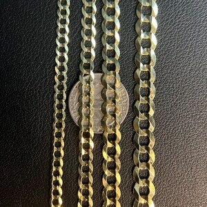 May include: Four gold chains of different widths, laid out side-by-side on a black surface. A silver coin is placed between the two middle chains.