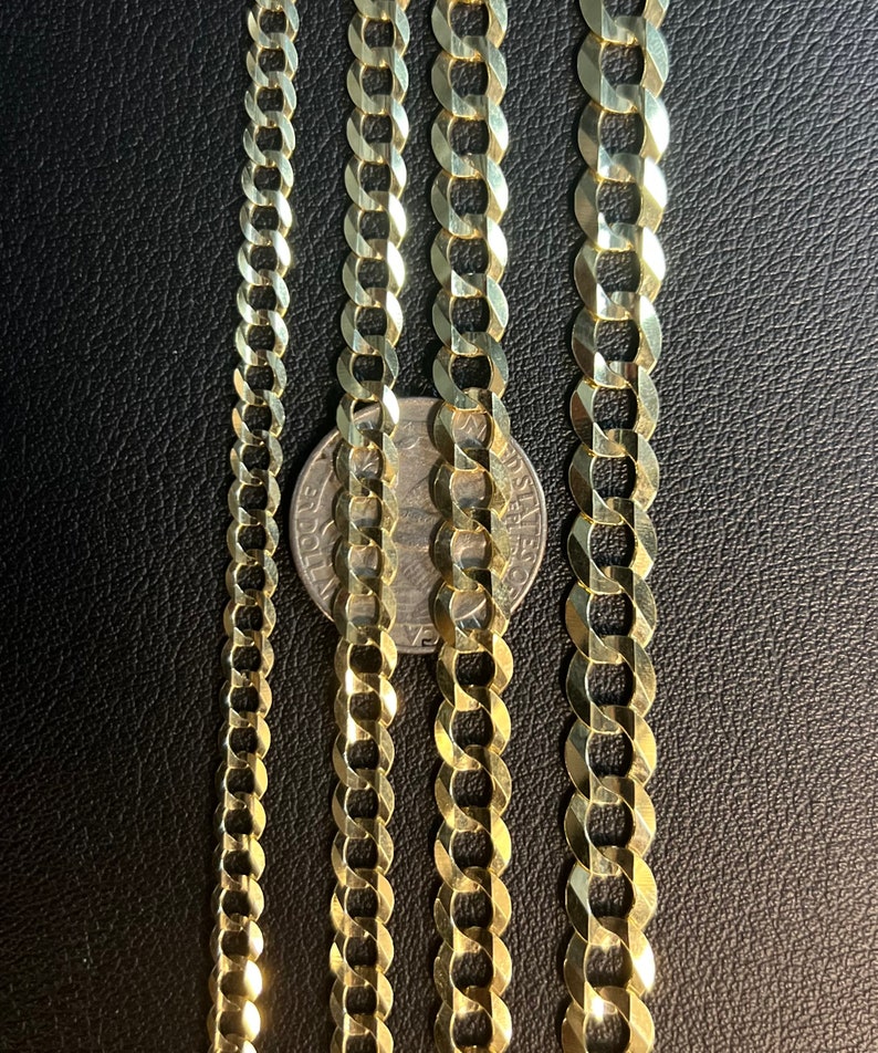May include: Four gold chains of different widths, laid out side-by-side on a black surface. A silver coin is placed between the two middle chains.