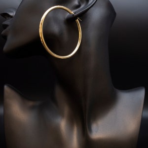May include: Gold hoop earrings on a black mannequin head.