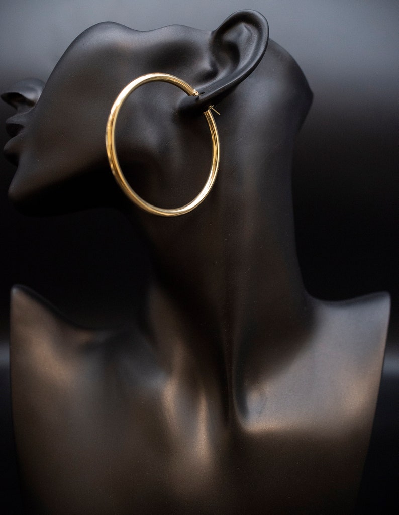 May include: Gold hoop earrings on a black mannequin head.