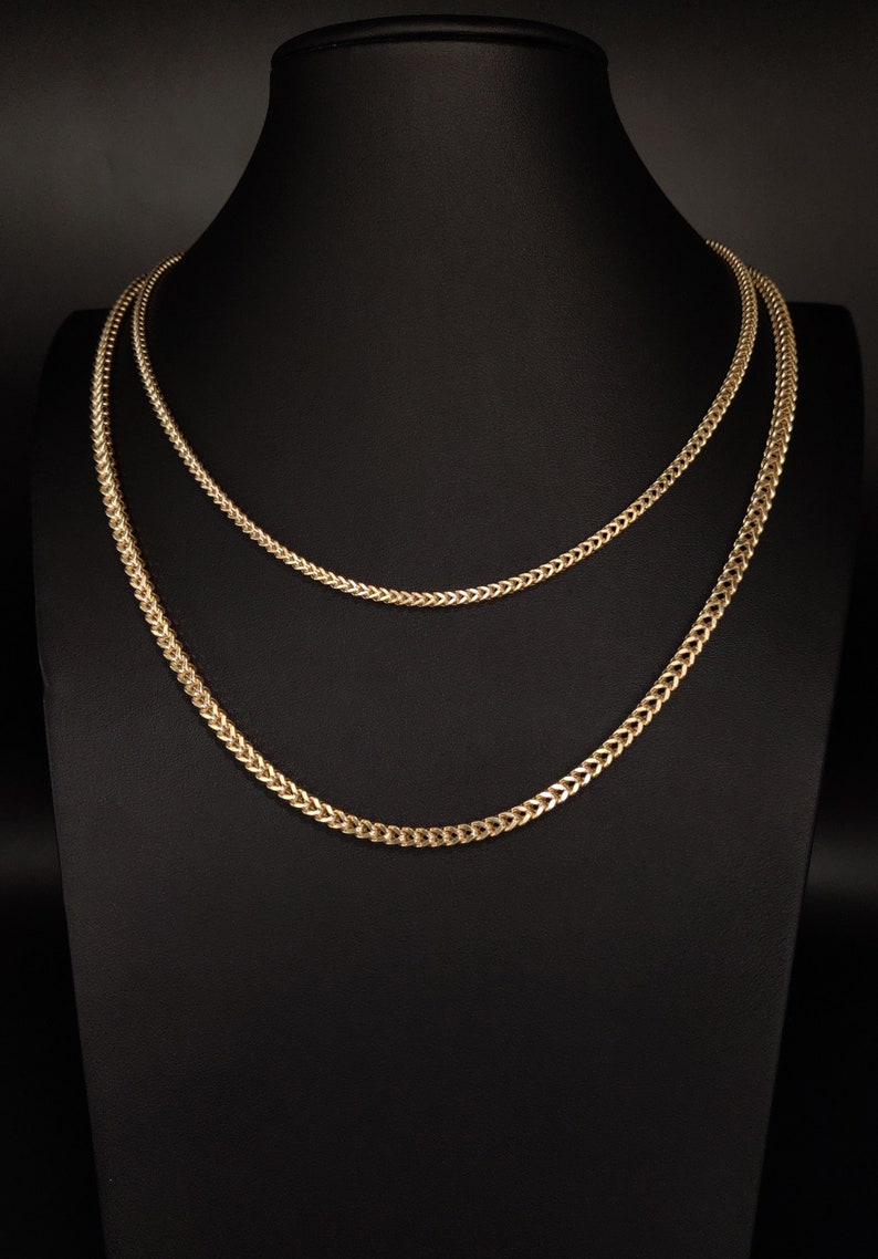 May include: Two gold chain necklaces on a black display stand. The chains are both the same style, but one is thicker than the other.