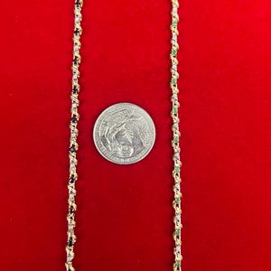 May include: Two gold chains with alternating black and green gemstones. The chains are on a red background. A US quarter is included for size reference.