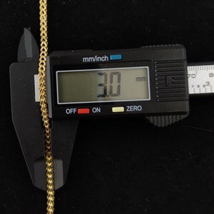 May include: Close-up of a gold chain measured with a digital caliper. The caliper reads 3.0 mm.