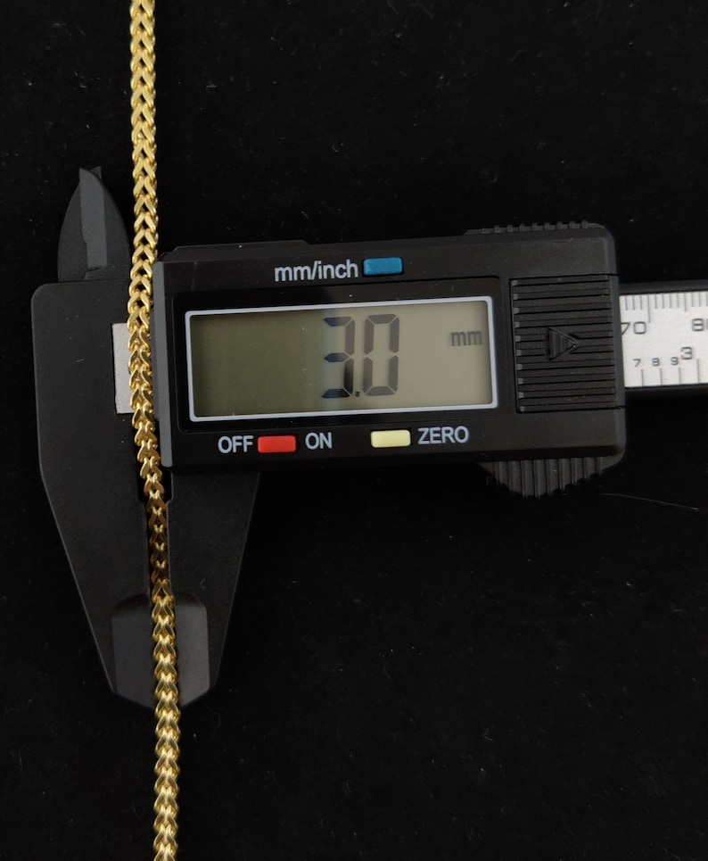 May include: Close-up of a gold chain measured with a digital caliper. The caliper reads 3.0 mm.