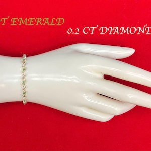 May include: A gold bracelet with green and white stones. The bracelet is on a white hand model. The text "1 CT EMERALD 0.2 CT DIAMOND" is visible in the image.