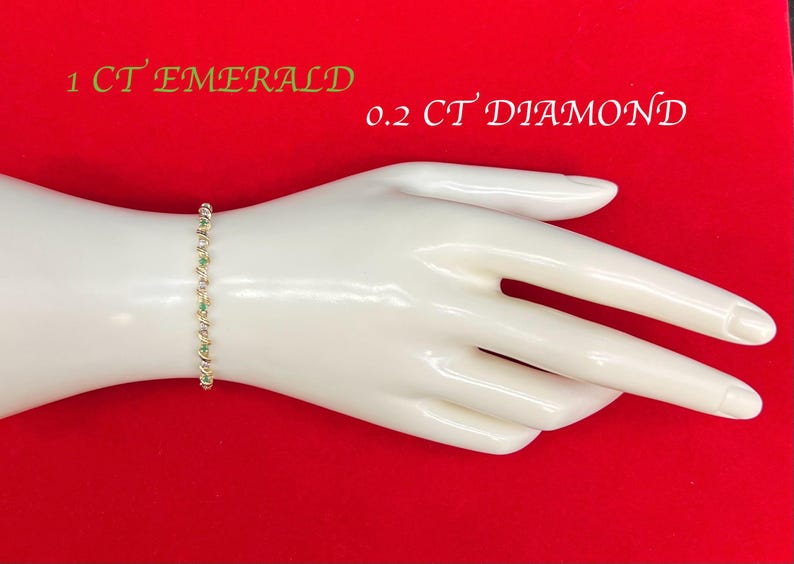 May include: A gold bracelet with green and white stones. The bracelet is on a white hand model. The text "1 CT EMERALD 0.2 CT DIAMOND" is visible in the image.