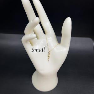 May include: A gold snake pendant necklace on a white mannequin hand. The word "Small" is written on the hand.