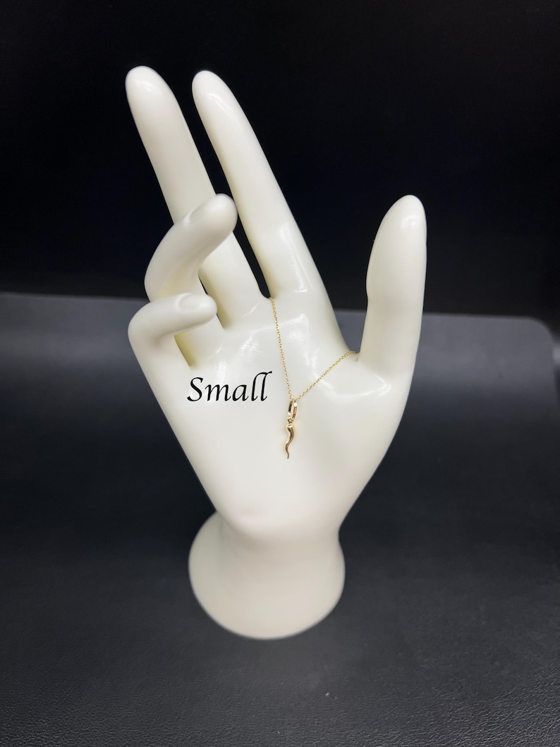 May include: A gold snake pendant necklace on a white mannequin hand. The word "Small" is written on the hand.