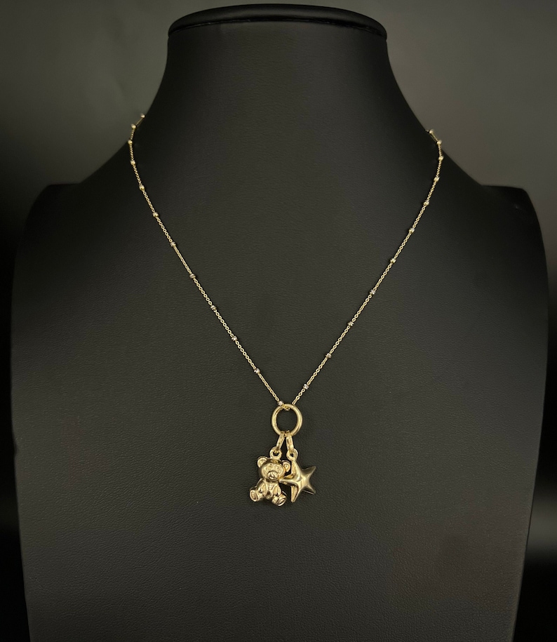 May include: A gold chain necklace with a small teddy bear and star charm.