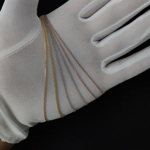 May include: Five different chain necklaces in gold, silver, and rose gold. The chains are laid out on a white surface.