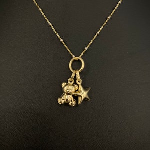 May include: A gold chain necklace with a small teddy bear charm and a star charm.
