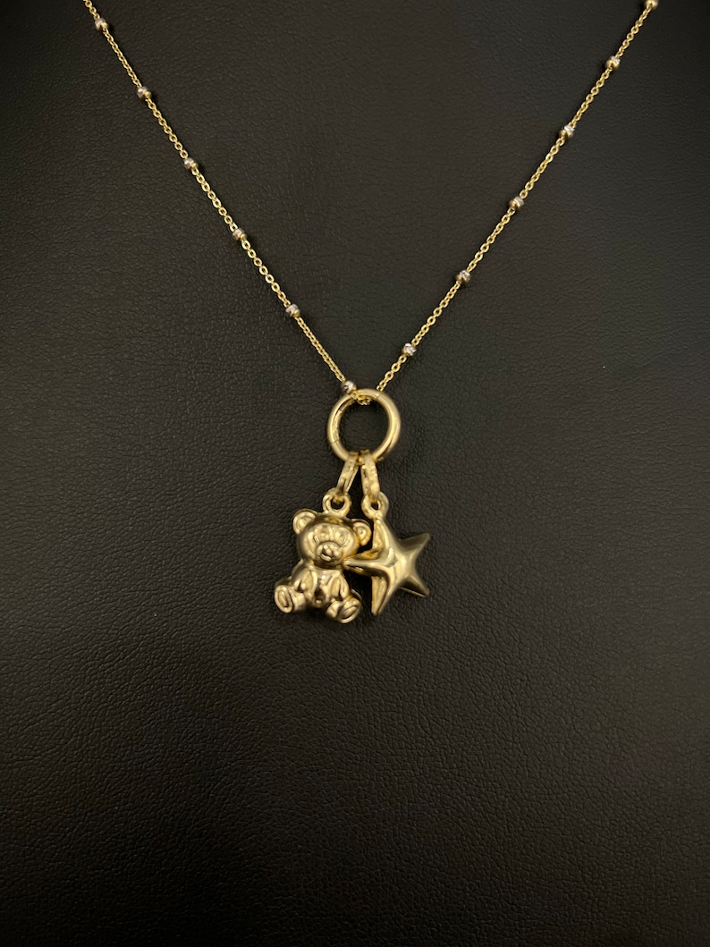 May include: A gold chain necklace with a small teddy bear charm and a star charm.
