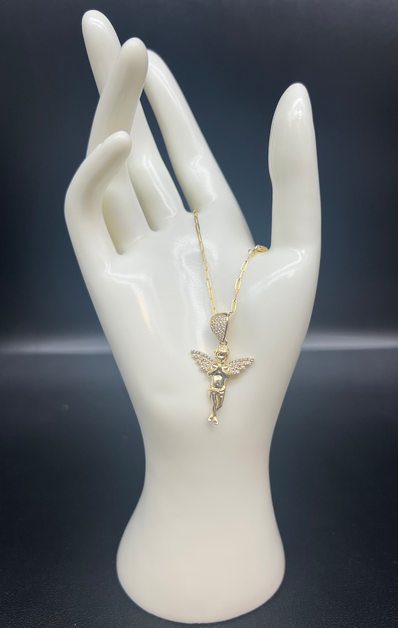 Puede incluir: Un collar de cadena de oro con un peque&ntilde;o colgante de &aacute;ngel detallado. El &aacute;ngel est&aacute; adornado con piedras de circonita c&uacute;bica transparentes.