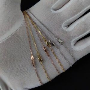 May include: A close-up of six different gold chains, including yellow gold, white gold, and rose gold, displayed on a white surface. The chains are all the same length and have a delicate, cable-link design.