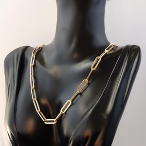 May include: A gold chain necklace with a link style and a pair of gold hoop earrings. The jewelry is displayed on a black mannequin bust.