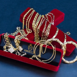Puede incluir: Una selecci&oacute;n de joyas de oro exhibidas en cajas de terciopelo rojo. La colecci&oacute;n incluye varios collares de cadena, pendientes de aro y una pulsera de estilo bamb&uacute;. La palabra "love" es visible en una de las cajas.