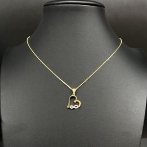 May include: A gold necklace with a heart-shaped pendant. The pendant incorporates an infinity symbol and is embellished with small, sparkling stones. The necklace is displayed on a black mannequin.