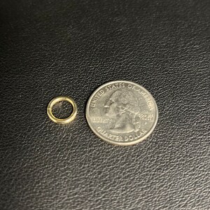 May include: A small gold jump ring next to a US quarter dollar coin. The jump ring is about the size of a dime.