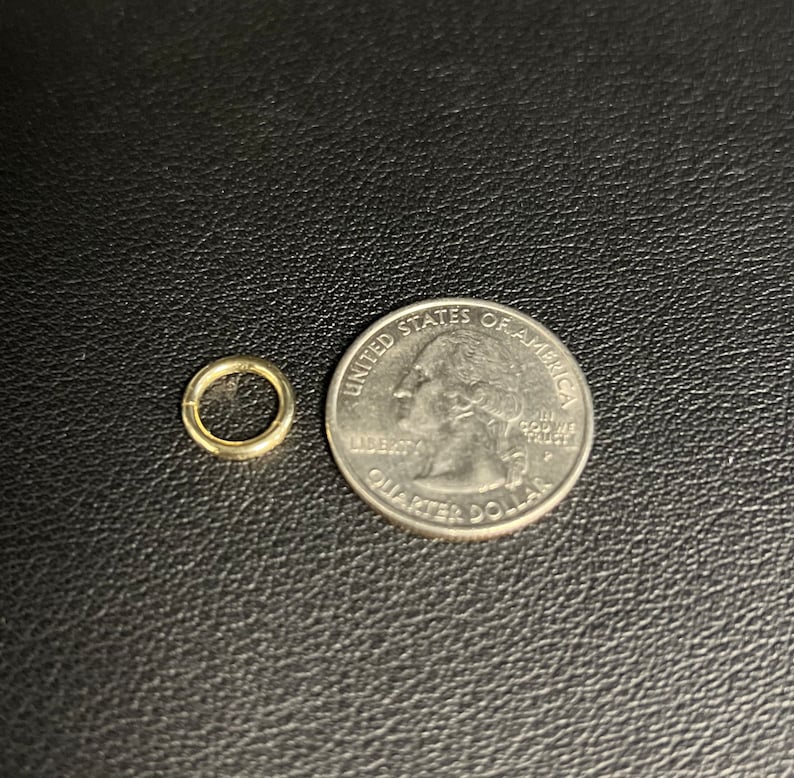 May include: A small gold jump ring next to a US quarter dollar coin. The jump ring is about the size of a dime.
